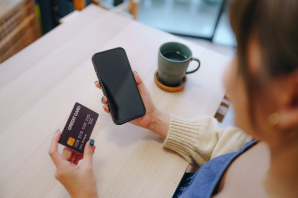 年轻的亚洲女子拿着信用卡，在家里用手机网购图片下载