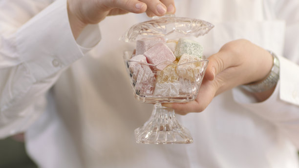 一个年轻女子的手拿着传统的东方美食，彩色的土耳其软糖在一个透明的玻璃碗。图片下载