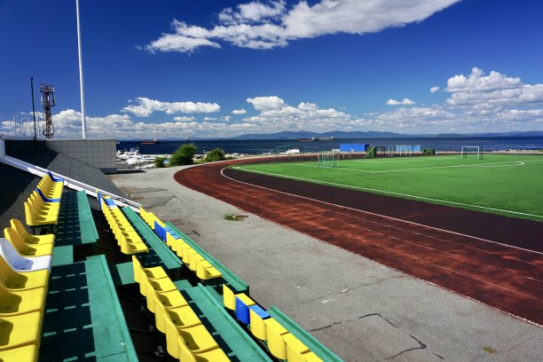 海边的足球场。足球场在晴朗的天气与云。海参崴的一个足球场，蓝天下，绿草如茵。图片下载