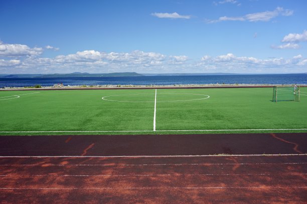 海边的足球场。足球场在晴朗的天气与云。海参崴的一个足球场，蓝天下，绿草如茵。图片下载