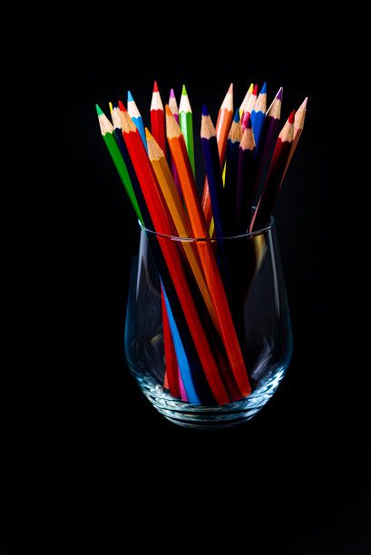 酒杯和水桶里的彩色铅笔。选择性模糊的一组彩色铅笔在酒杯上孤立的白色或黑色背景，现代艺术。现代图片下载
