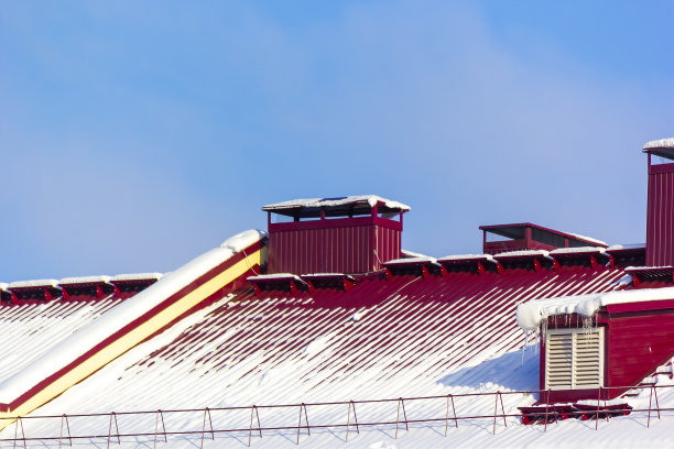 雪中房子的红色屋顶。象征新年假期，圣诞节和圣诞老人的到来。有烟囱的屋顶上有积雪。图片下载