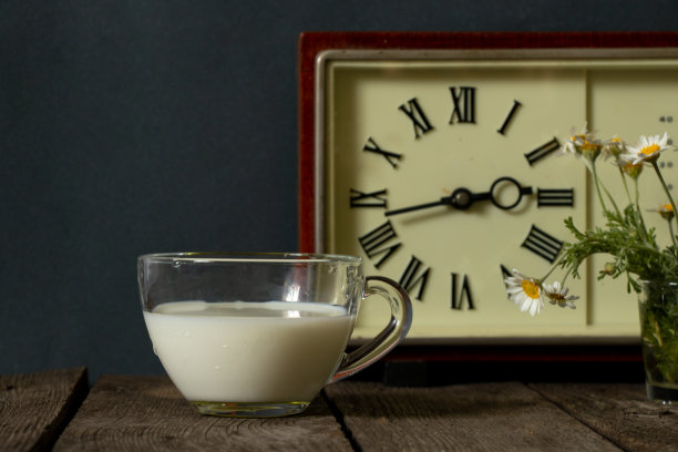 一杯牛奶和一个插着雏菊的花瓶，放在厨房木桌上的时钟旁边图片下载