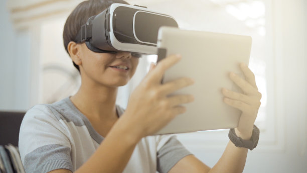 十几岁的女子戴着虚拟现实眼镜，在客厅使用平板电脑。图片下载