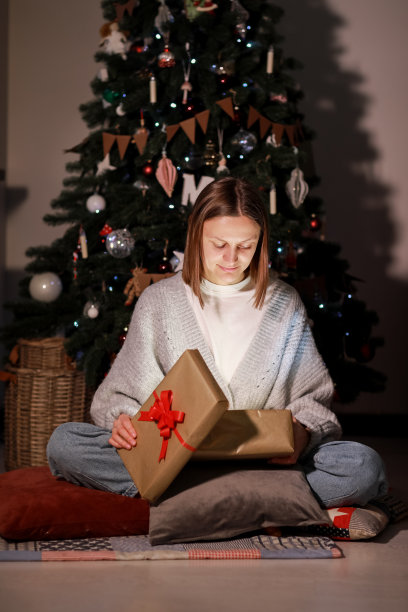 圣诞节的魔力。惊奇的年轻美丽的女人打开圣诞礼盒里面的光，坐在地板上靠近圣诞树在家里。高质量照片图片下载