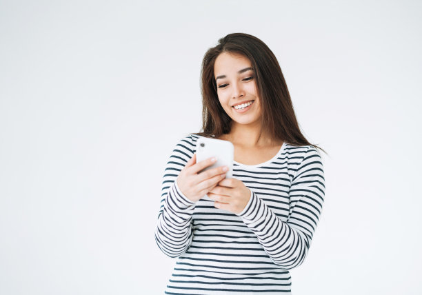 年轻快乐的亚洲女人长头发在条纹长袖使用手机在白色背景隔离图片下载