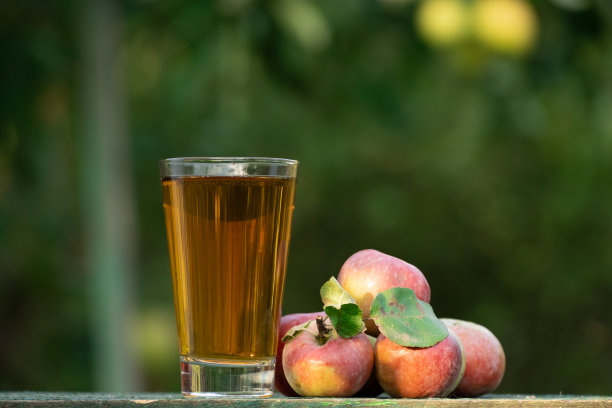 苹果汁放在花园里的木桌上，周围都是苹果。农夫拿着一个罐子，把苹果园里的新鲜果汁倒进杯子里。把苹果汁倒进玻璃杯里图片下载