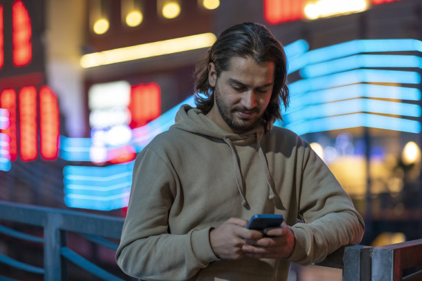 英俊的年轻人在街上的霓虹灯前发短信图片下载
