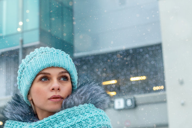 一个戴着帽子和围巾的年轻女子在冬天的雪城。满怀希望地展望未来。特写镜头图片下载