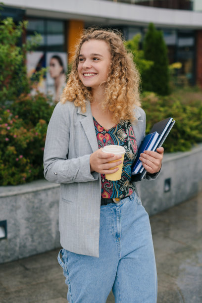 女学生站在大学校园，拿着一杯咖啡和一台笔记本电脑，在演讲后喝咖啡休息。享受大学生活。学习教育理念。图片下载