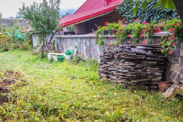 花园用具附近的房子有一个美丽的红色屋顶。乡村房子附近的花园。栅栏附近用来给花园浇水的水壶图片下载