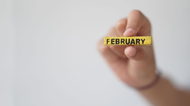 特写镜头，一只手在白色背景下拿着一个二月的方块。图片下载