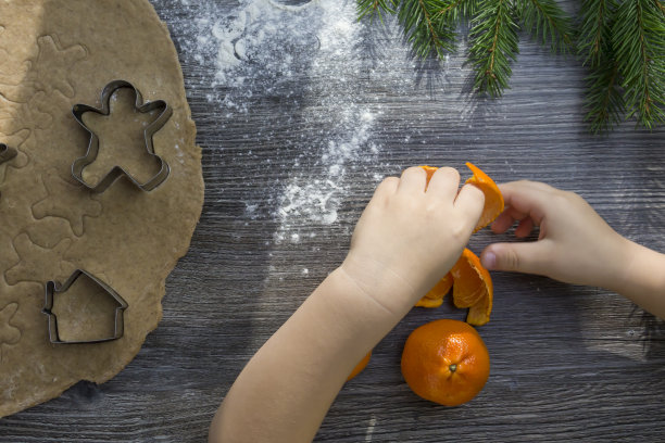 新年和圣诞节装饰在一个木制表面上的橘子和一棵圣诞树。平安夜，一个小孩一边吃橘子，一边做姜饼。图片下载
