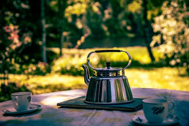 特写镜头是一个茶壶和两个杯子放在公园的木制野餐桌上，背景模糊图片下载