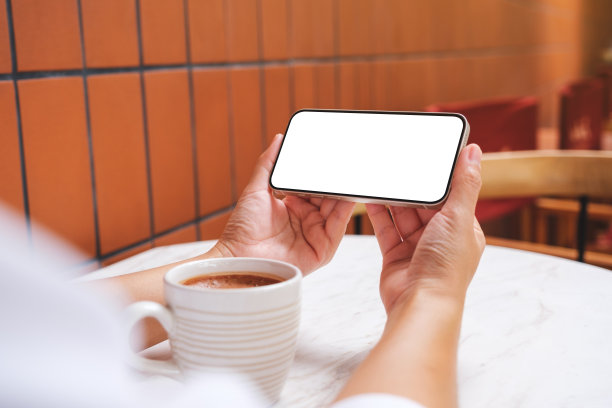 一个女人拿着空白桌面屏幕的手机，咖啡杯放在桌子上的模型图像图片下载