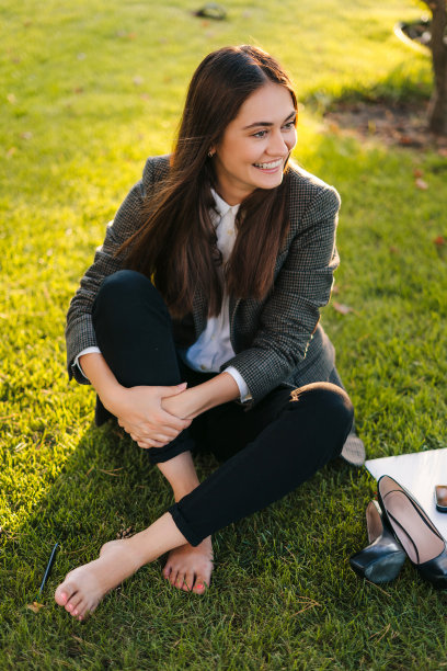 年轻的独立女性在辛苦工作一天后在公园的草地上放松，坐在舒适放松的姿势。暑假旅游度假娱乐。夏天的本性。绿色的大自然。图片下载