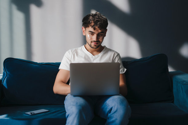 有魅力的年轻人在家里的沙发上放松，拿着笔记本电脑，使用和工作，在客厅里度过他的空闲时间。教育互联网技术。互联网通信。舒适的公寓。图片下载