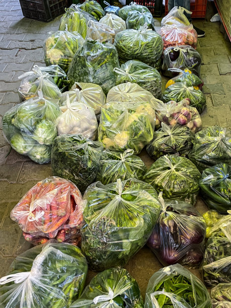 市场摊位展示的新鲜蔬菜生产在大塑料捆绑袋交付在人行道上，菜花，卷心菜，胡萝卜，土豆和红洋葱，高架视图，重点在前景图片下载