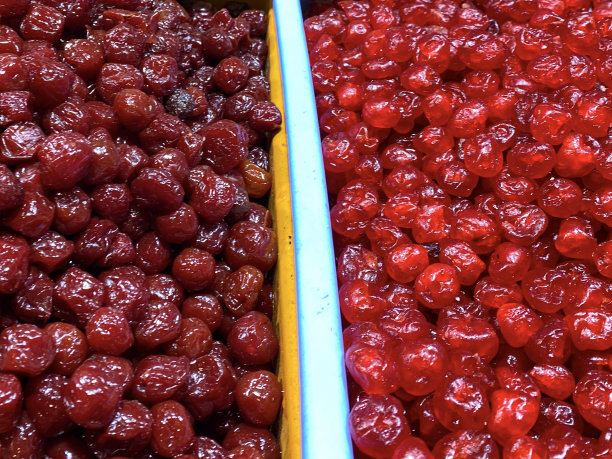 市场摊位展示的塑料容器装满了成堆的干果，准备按重量出售，蜜饯(糖霜)樱桃，健康食品零食，高架视图，重点在前景图片下载