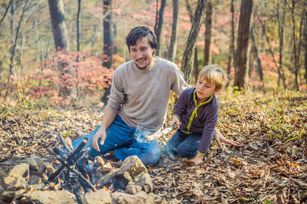 父亲和兴奋的儿子坐在帐篷里在森林野营篝火图片下载