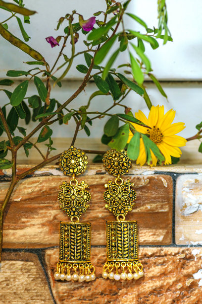 印度风格的现代金耳环与珍珠补丁挂在墙上的叶子和花。金色Jimikki库存照片与绿叶和花。图片下载