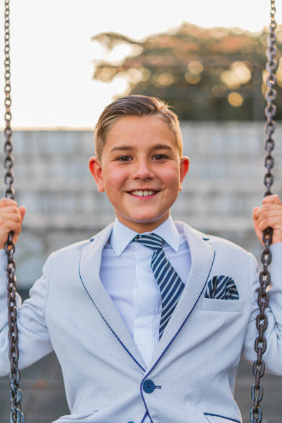 一个穿着正装的可爱男孩在秋千上摆姿势的垂直镜头图片下载