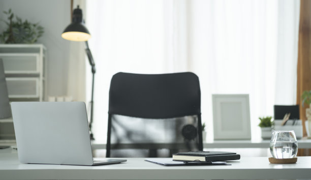 笔记本电脑，一杯水，在明亮的现代办公室的白色桌子上。图片下载