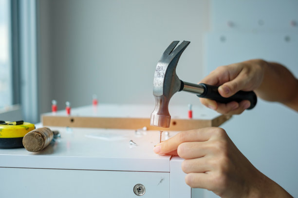 一名男子用锤子把钉子敲进木板，在家里组装或修理家具。DIY，装修，维修和开发住宅或公寓概念图片下载