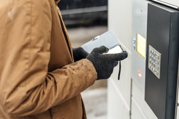 在自助邮件终端机旁，一名手持手机的男子。包裹投递机。拿着智能手机的人。邮件递送和邮政服务，网上购物，电子商务概念图片下载