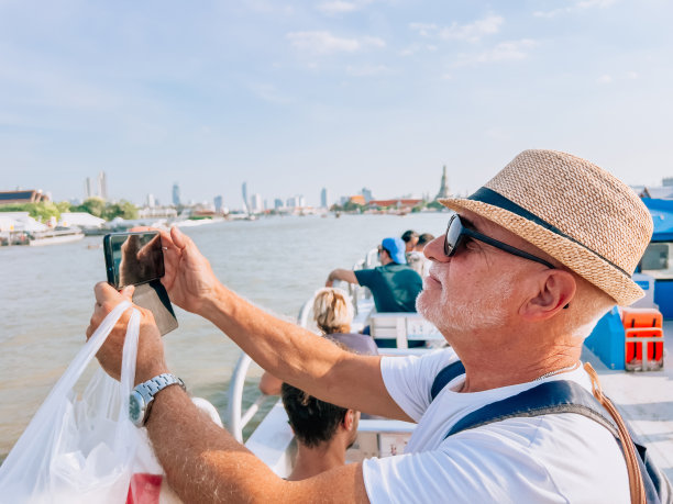 一位年长的男子在曼谷市的渡轮旅行中使用手机图片下载