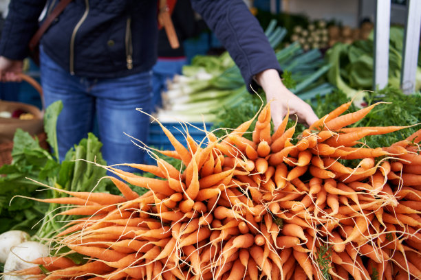 妇女在农贸市场挑选新鲜的胡萝卜和蔬菜图片下载