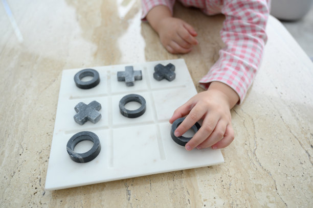 特写手的孩子小女孩玩Tic Tac Toe或牛棋盘游戏在大理石桌子上，俯视图。图片下载