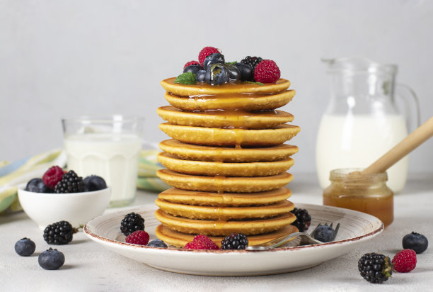 早餐是丰盛的煎饼，盘子里有浆果浇在蜂蜜上，杯子和罐子里有牛奶图片下载