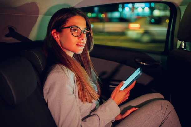 一位商务女性晚上坐在汽车后座上使用智能手机图片下载