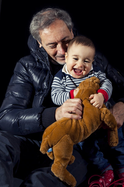 微笑的小男孩拥抱他的父母坐在黑色背景的肖像图片下载