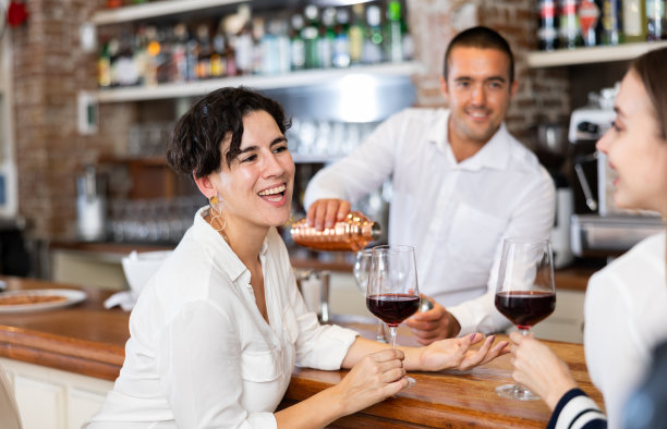 两个女朋友坐在餐厅的吧台边聊天边喝红酒图片下载