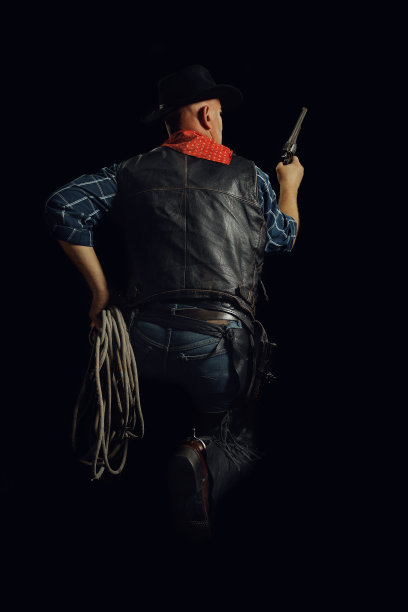 牛仔蹲着，握着绳子和枪的背影图片下载