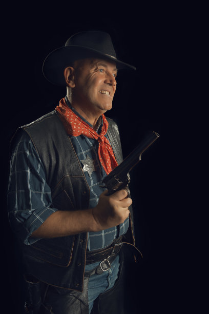 一位老牛仔站在黑色背景前，手持左轮手枪大喊大叫图片下载