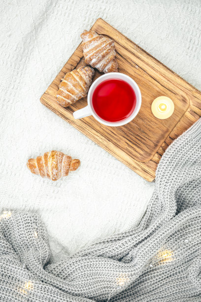 一杯茶，一支蜡烛，一个羊角包和一个针织元素在床上，俯视图。图片下载