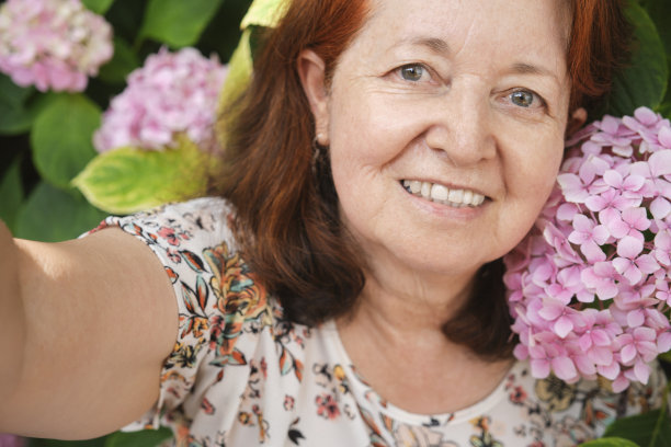 一个快乐的成熟的西班牙女人在花园的自拍照，周围是粉红色的花。图片下载