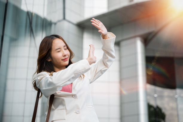 快乐的女人穿着白色西装外套和棕色的包在阳光明媚的户外图片下载