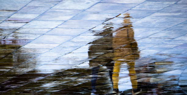 在雨天，无法辨认的人走在潮湿的城市街道人行道上的抽象模糊剪影反射图片下载