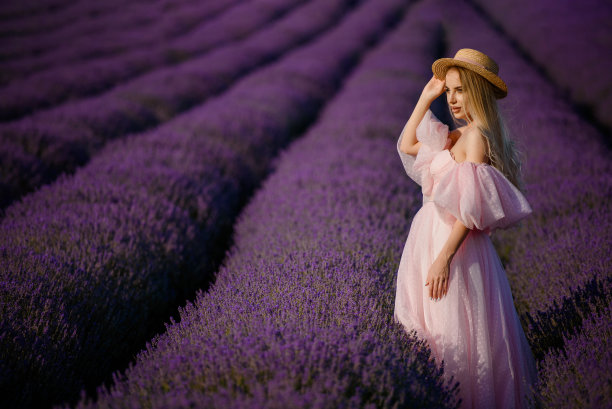 一位年轻美丽的女子，穿着粉红色的连衣裙，戴着一顶帽子，走在薰衣草田里。图片下载