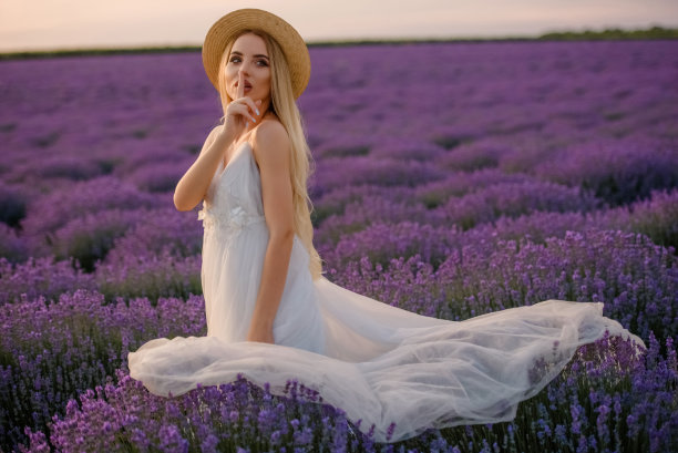 一个年轻美丽的女人，穿着白色的裙子，戴着一顶帽子，走在薰衣草田。图片下载