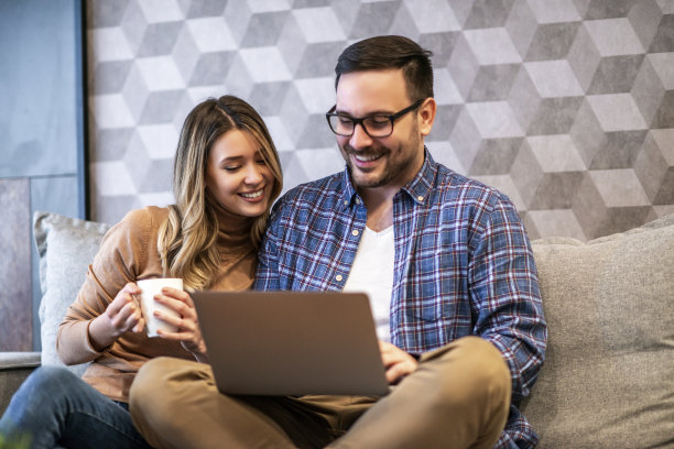 欢快的情侣在使用笔记本电脑时一起微笑图片下载