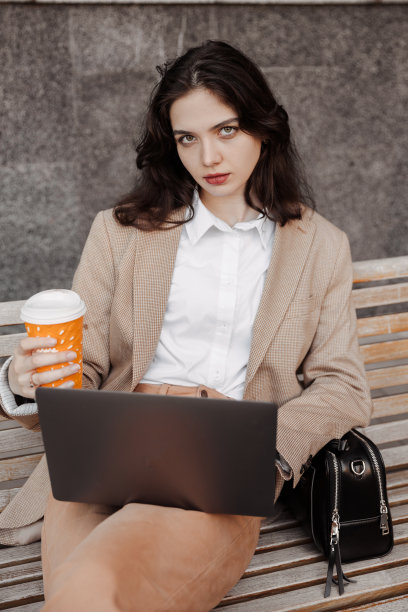 年轻的女商人坐在长凳上，拿着笔记本电脑的现代办公大楼背景图片下载