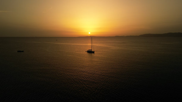 迷人的场景，一艘帆船在大海中间与橙色日落的场景图片下载