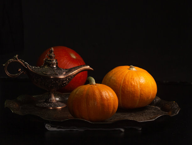 黄橙色的南瓜蜡烛托盘，黑色背景上的阿拉丁灯，万圣节的概念和秋收南瓜的特写复制空间图片下载