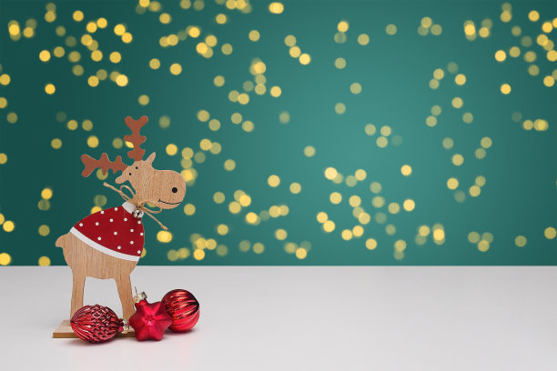 白色的桌子上有一只带球的木制圣诞驯鹿，背景是模糊的散景。背景为绿色。模糊的光金色散景。图片下载