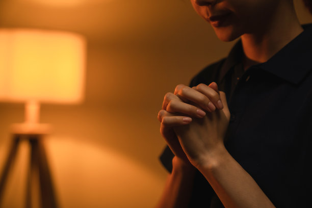 女人的手祈祷与神奇的光流动通过橙色散景背景。图片下载